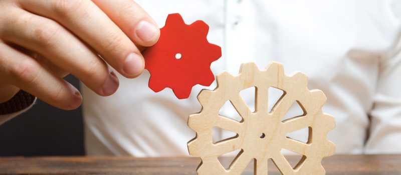 Businessman connects a small red gear to a large gear wheel. Symbolism of establishing business processes and communication. Increase efficiency and productivity. The best business formula for success